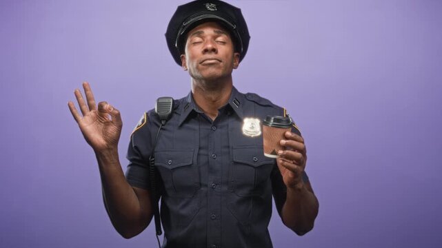 Police officer man wearing uniform and cap holding a takeaway coffee cup and making an ok sign with his hand in studio; calm reflection.