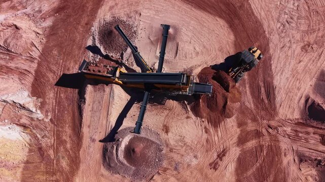 Vertical aerial view of a mobile screening plant separating clay and soil fractions in an open quarry, while a wheel loader removes processed material for transport or stockpiling