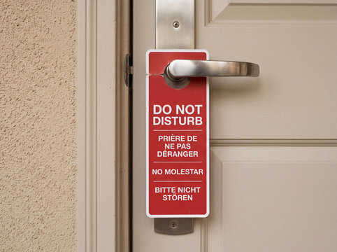 Red multilingual Do Not Disturb sign on a hotel door handle in English, French, Spanish, and German. Close up