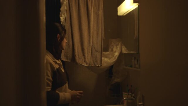 Woman standing in bathroom opening medicine cabinet and reaching for personal care products, everyday hygiene routine in home interior