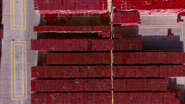Vertical aerial view of palletized crates containing bottled carbonated beverages stored in dense rows at an industrial distribution yard within a beverage production supply chain