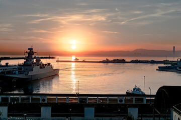 Obraz premium Sunrise at the L'Espadon scuba diving club in the Port of Algiers with an Admiralty ship and trawlers moored and sailing in the sea bay with seagulls flying and the great mosque minaret in background.