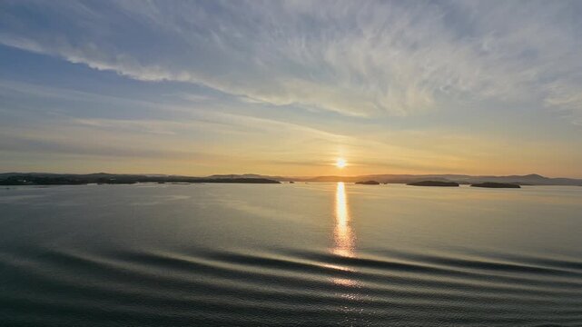 Sonnenuntergang der sich im Wasser spiegelt, mit leicht bedecktem Himmel, im Vordergrund sanfte Wellen, Bergen, Vestland, Norwegen, Europa