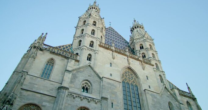 Cinematic low angle gimbal panorama of the Gothic St. Stephen's Cathedral front facade at dusk in Vienna, Austria. Detailed view of the illuminated architecture and towers against the twilight sky