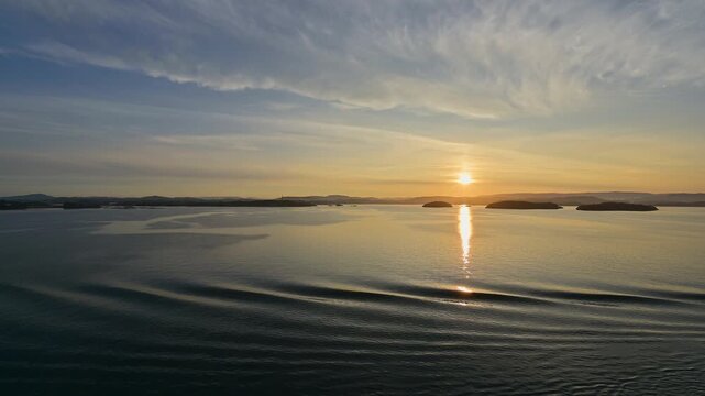 Sonnenuntergang der sich im Wasser spiegelt, mit leicht bedecktem Himmel, im Vordergrund sanfte Wellen, Bergen, Vestland, Norwegen, Europa