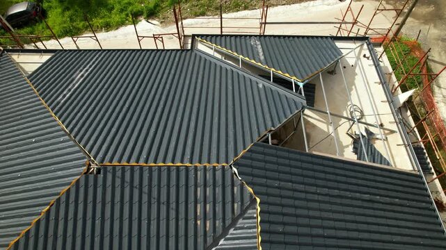 Installation of anthracite metal roofing tiles on a complex building. High-angle drone footage showing the progress of the installation at the construction site. Innovative insulation materials.