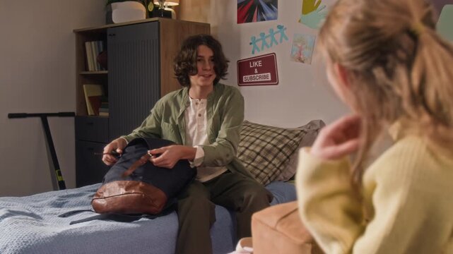 Rack focus view of teenage boy chatting with younger sister and buttoning his bag getting ready for school day, girl checking her backpack