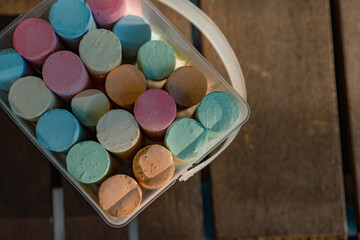 Sidewalk chalk in a plastic bucket on a wooden table
