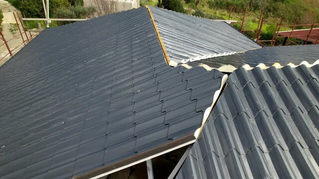 Installation of anthracite metal roofing tiles on a complex building. High-angle drone footage showing the progress of the installation at the construction site. Innovative insulation materials.