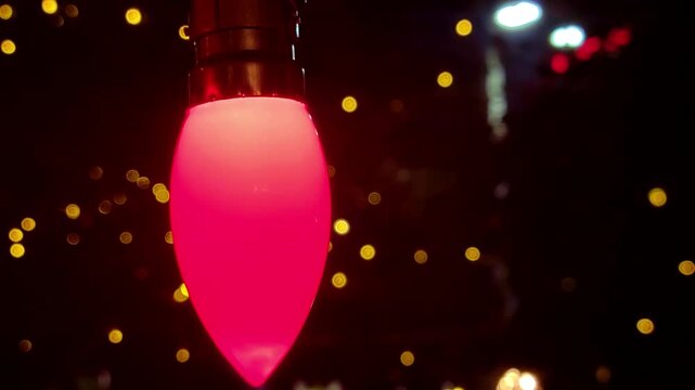 A slowly spinning C7 red Christmas light bulb is in focus, with a blurred background of warm yellow bokeh lights.