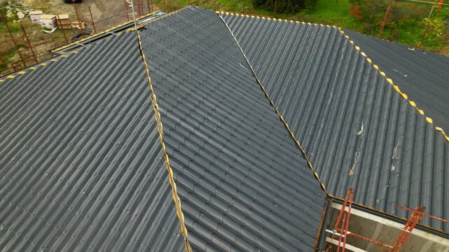 Installation of anthracite metal roofing tiles on a complex building. High-angle drone footage showing the progress of the installation at the construction site. Innovative insulation materials.