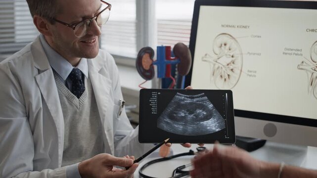 Over shoulder of urologist presenting ultrasound scan on tablet and discussing kidney condition with elderly patient during medical appointment in contemporary office