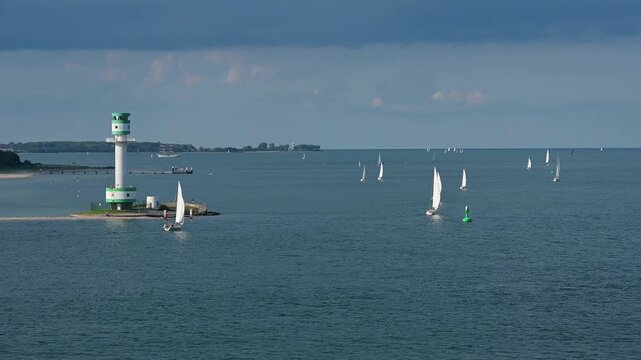 Mehrere Segelboote und Schiffe auf ruhigen blauen Meer unter einem bew&ouml;lkten Himmel mit einem Leuchtturm im Hintergrund, Leuchtturm Friedrichsort, Kieler Bucht, F&ouml;rde, Ostsee