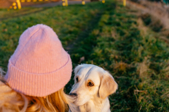 Gentle female, blonde Caucasian, sharing quiet eye contact with golden retriever in sunset light