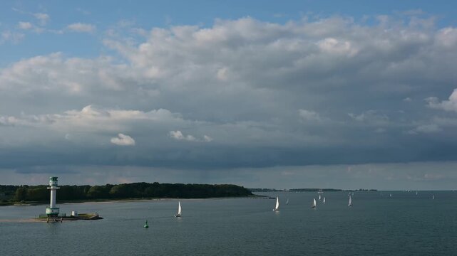 Mehrere Segelboote und Schiffe auf ruhigen blauen Meer unter einem bew&ouml;lkten Himmel mit einem Leuchtturm im Hintergrund, Leuchtturm Friedrichsort, Kieler Bucht, F&ouml;rde, Ostsee