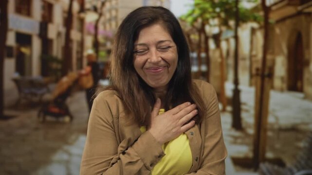 Woman wearing yellow shirt touches chest on a busy city street with blurred storefronts; gratitude sincerity.