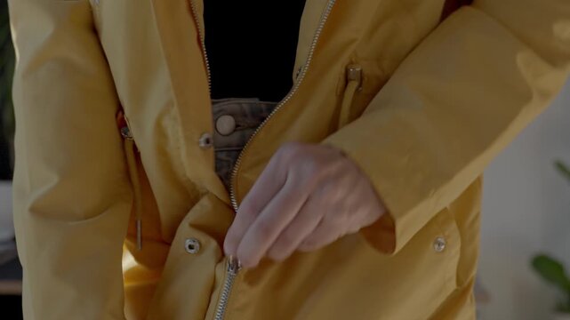 Closeup of hands zipping yellow jacket over black top and light denim jeans. Concept of daily dressing routine and outerwear preparation