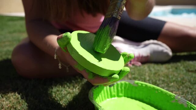 Young girl painting a green tejo game piece