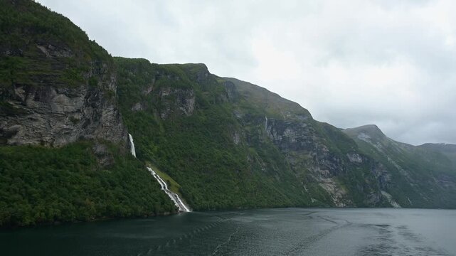 Geiranger Fjord mit Wasserfall umgeben von Felsen und Bergen mit bedecktem Himmel, Geirangerfjord, Geirnanger, Stranda, Romsdal, Norwegen, Europa