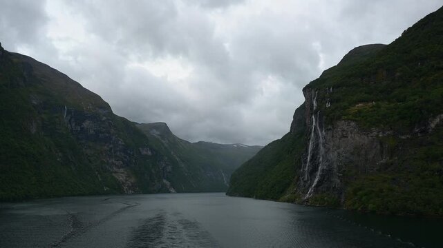 Geiranger Fjord mit Wasserfall umgeben von Felsen und Bergen mit bedecktem Himmel, Geirangerfjord, Geirnanger, Stranda, Romsdal, Norwegen, Europa