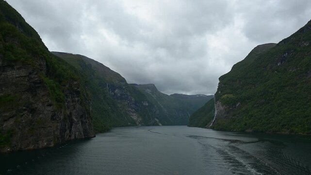 Geiranger Fjord mit Wasserfall umgeben von Felsen und Bergen mit bedecktem Himmel, Geirangerfjord, Geirnanger, Stranda, Romsdal, Norwegen, Europa