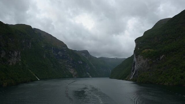 Geiranger Fjord mit Wasserfall umgeben von Felsen und Bergen mit bedecktem Himmel, Geirangerfjord, Geirnanger, Stranda, Romsdal, Norwegen, Europa