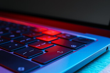 Stylish modern laptop in neon lights on wooden table, closeup
