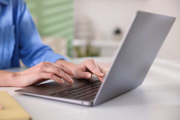 Woman working on laptop at white table indoors, closeup