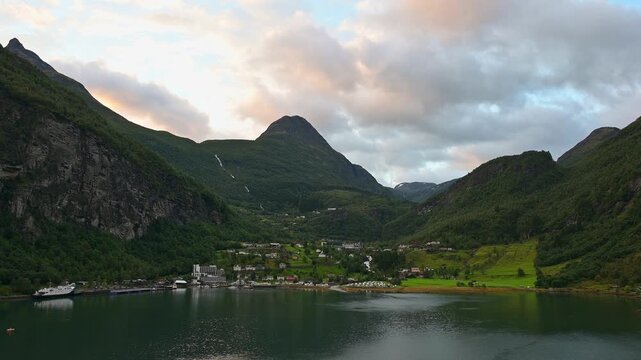 Bergige Landschaft mit einem ruhigen Fjord, in dem die umliegenden Berge und das Dorf reflektiert werden, umgeben von gr&uuml;ner Natur, Geirangerfjord, Geiranger, Stranda, Romsdal, Norwegen, Europa