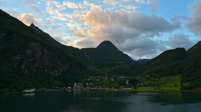 Bergige Landschaft mit einem ruhigen Fjord, in dem die umliegenden Berge und das Dorf reflektiert werden, umgeben von gr&uuml;ner Natur, Geirangerfjord, Geiranger, Stranda, Romsdal, Norwegen, Europa