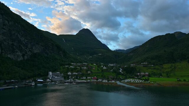 Bergige Landschaft mit einem ruhigen Fjord, in dem die umliegenden Berge und das Dorf reflektiert werden, umgeben von gr&uuml;ner Natur, Geirangerfjord, Geiranger, Stranda, Romsdal, Norwegen, Europa