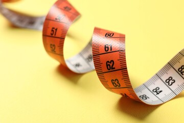 One measuring tape on yellow background, closeup