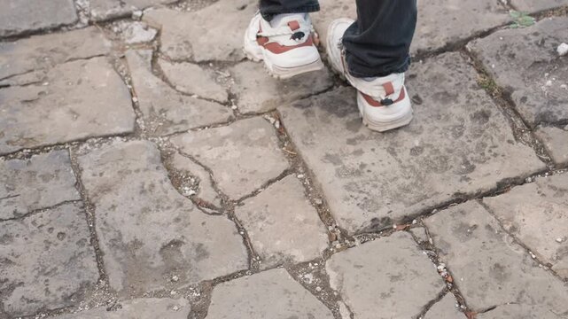 Closeup of sneakers walking on stone pavement, white patterned shoes stepping over weathered cobblestones with crevices and moss, rhythmic stride and balanced motion, texture details and ground