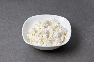 Cottage cheese in a white bowl on a gray surface in a kitchen setting showing fresh dairy food ready to serve