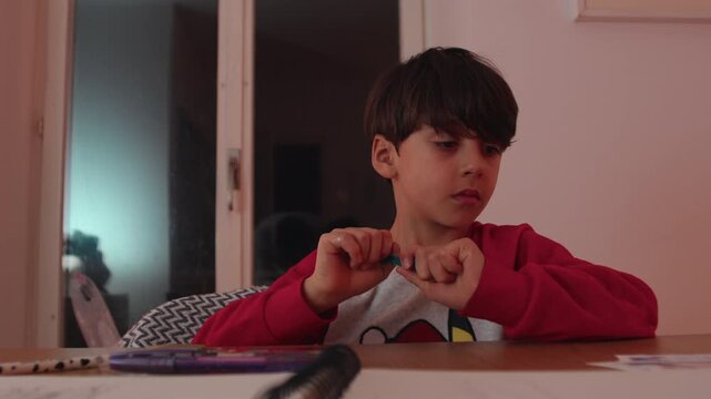 Boy concentrating on small paper card while writing at table, schoolwork scene inside home with thoughtful expression and steady hand