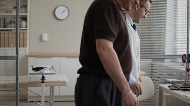 Eye level side view medium tracking shot of male urologist and senior patient shaking hands, sitting at consultation desk before medical appointment in professional clinic environment