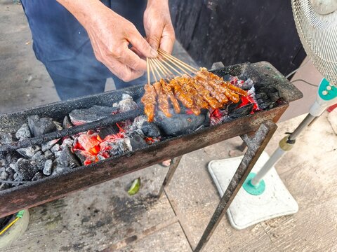 Close-up of a street food vendor grilling traditional Indonesian chicken satay (sate ayam) over hot charcoal.