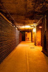 Fototapeta premium Visit of deep and long underground caves with dusty bottles on racks, traditional method making champagne sparkling wine in Reims, Champagne, France