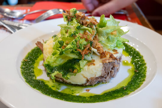 French dish parmentier of candied duck, shredded canard confit with potatoes puree and green pesto, served in traditional bistro bouillon restaurant in Paris