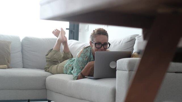 Adult woman using laptop at home in casual clothes, relaxed lifestyle moment with technology, remote work and smart working concept, browsing internet, chatting online, social media use and digital li