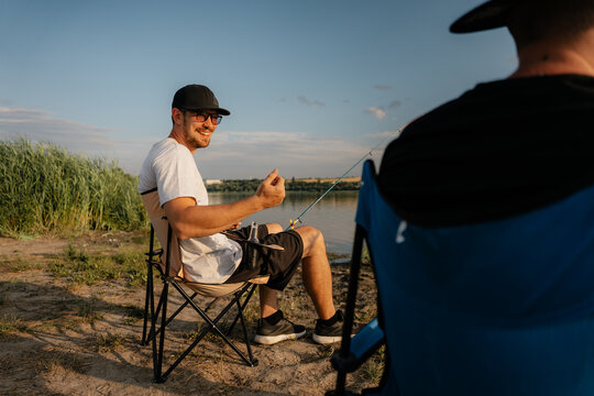 Two friends fishing and relaxing on a lake shore on a warm summer evening
