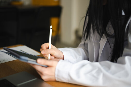 A person in a white shirt uses a stylus to write on a tablet, with papers and a laptop on the desk.