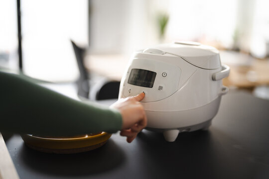 A person's hand presses a button on a modern kitchen appliance, selecting a cooking function.