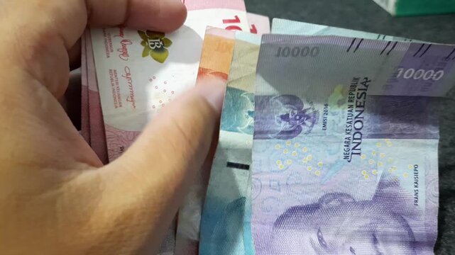 a person holding a stack of Indonesian Rupiah banknotes  The visual of cash money can symbolize various financial themes such as salary, savings, profit, expenses, inflation
