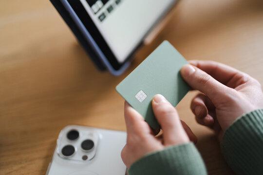 A person holds a payment card near a tablet and smartphone, ready to make a transaction.