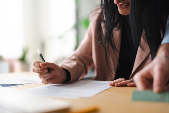 A woman signs a document while another person's hand is visible, suggesting a business transaction or agreement.