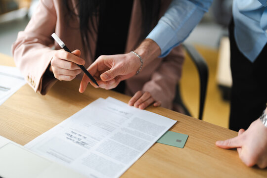 A woman signs a document while a man points to the paper, indicating collaboration and agreement in a business setting.
