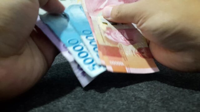 a person counting Indonesian Rupiah banknotes, illustrating concepts related to finance, economy, business transactions, income management, and daily life