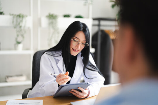 A medical professional in a white coat uses a stylus to interact with a tablet while consulting with a patient in a modern office setting.
