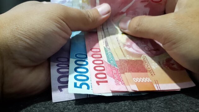 a person holding a stack of Indonesian Rupiah banknotes, representing concepts related to business, economy, finance, income, spending, and everyday life